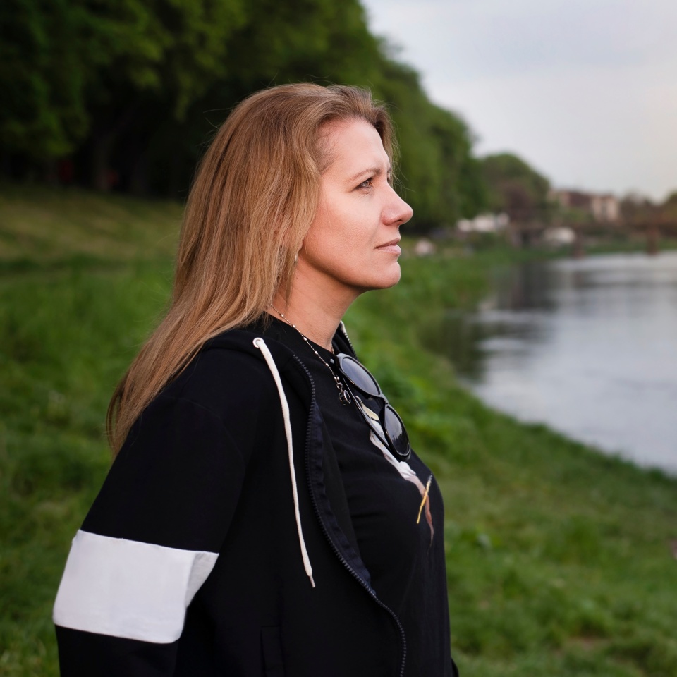 A mature woman with a happy face looks into the distance and enjoys the peace and quiet of the river in the evening. The woman is dreaming and gaining new strength, praying at sunset