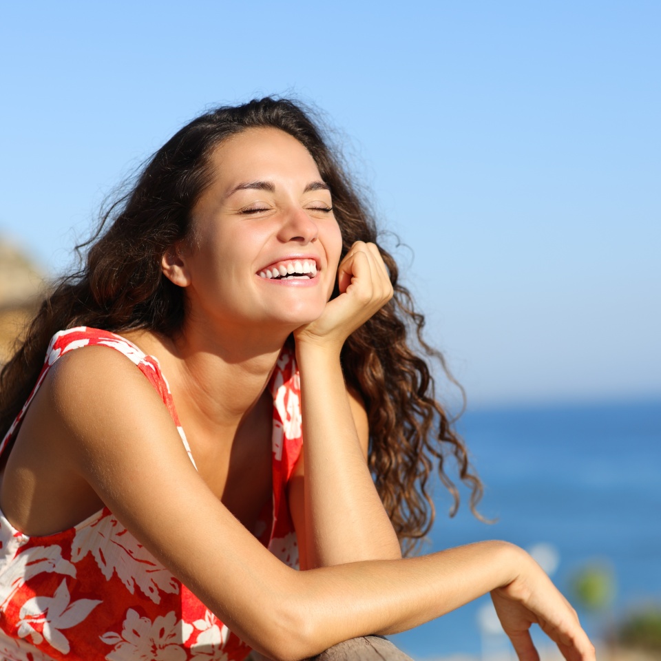 Happy woman in red dress laughing on the beach