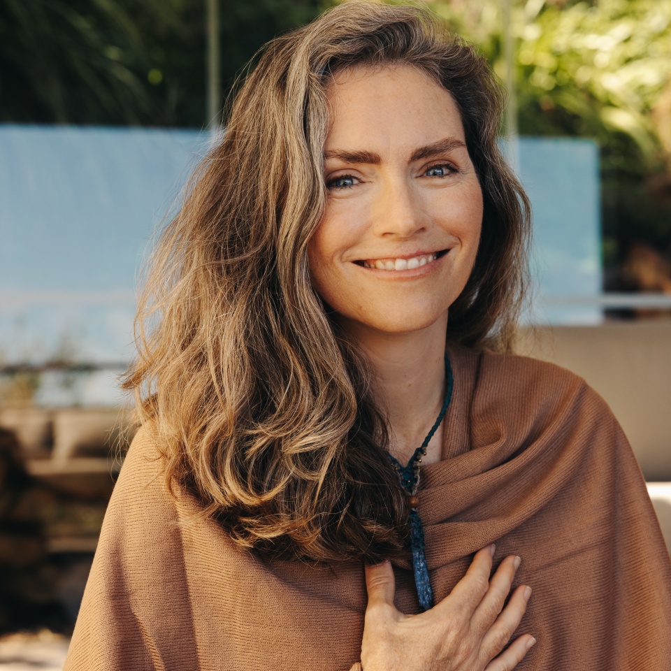 Cheerful senior woman smiling at the camera while wearing a crystal necklace. Happy woman meditating and practicing crystal healing on her chest chakra. Mature woman following a holistic lifestyle.