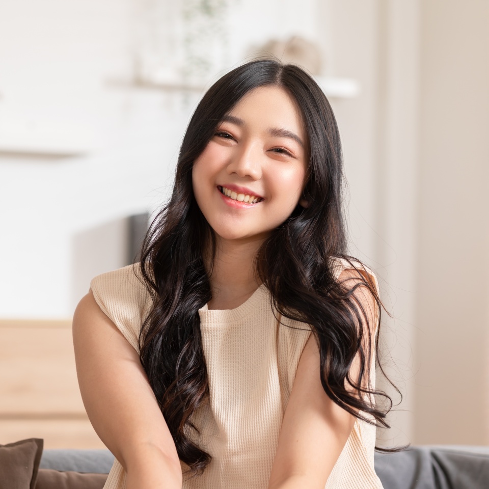 Stunning Beautiful Attractive Asian young woman sit on couch or sofa looking at camera and smile happiness and comfortable at home.Cute girl smile cross arm confident and relax in living room