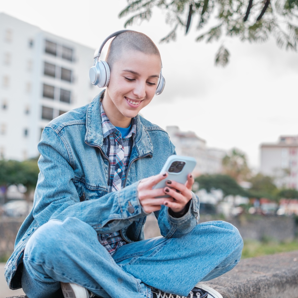 Young woman with short hair using her smartphone while listening to music outdoors and smiling. Concept: Freedom, lifestyle, urban style