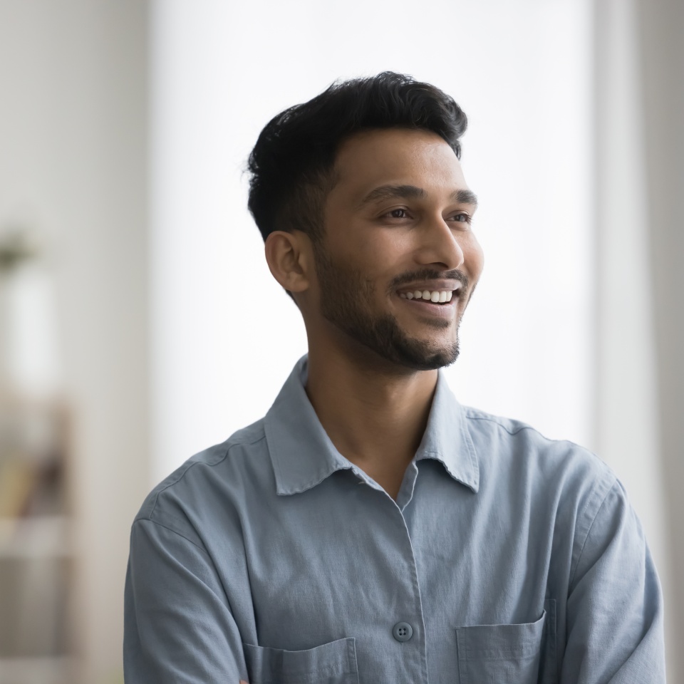 Happy successful handsome young Indian man casual indoor portrait. Positive confident professional, business man, entrepreneur in casual shirt looking at window away with toothy smile