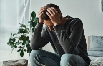 upset bearded man in casual home wear touching head while sitting on bed at home, depression