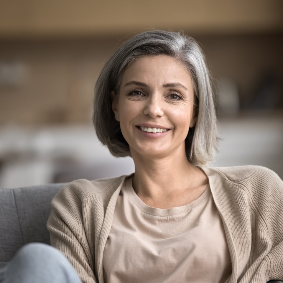 Close up portrait of smiling mature woman looking at camera, pose for photo, relax on cozy couch in living room, feels carefree on weekend alone indoors, pleasant happy lady enjoy leisure time at home