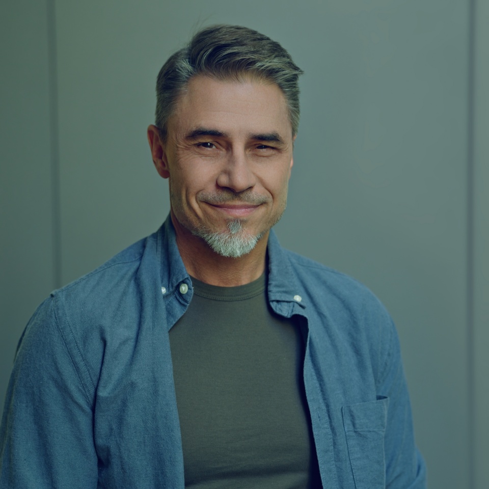 Confident, happy middle-aged man portrait with a calm cheerful, smiling expression against a grey wall background with copy space.
