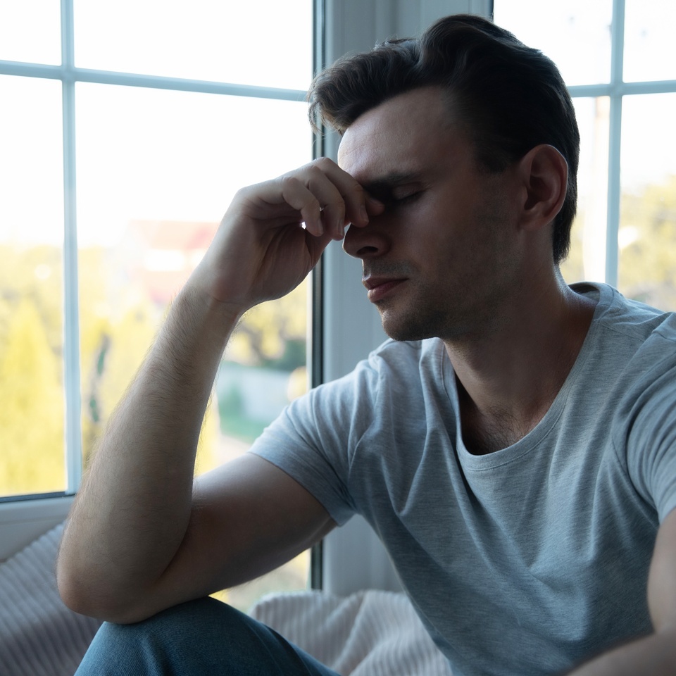 Depressed, sad, frustrated, crying, scared, instability mental and bipolar young man sitting on the windowsill at home. Headache because overworked and stress