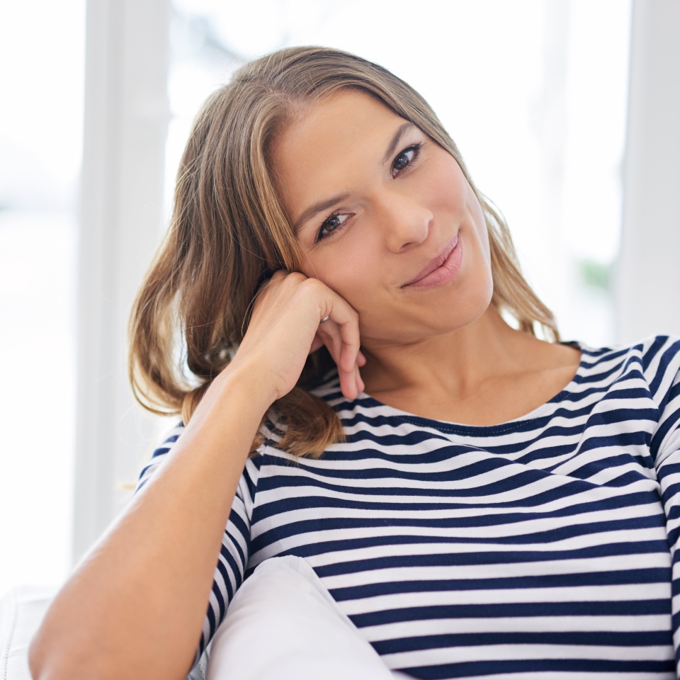 Portrait, house and woman on sofa, comfort and happiness with weekend break, relax and peaceful. Face, apartment and cheerful person on couch, girl and joyful with wellness, calm or resting in lounge