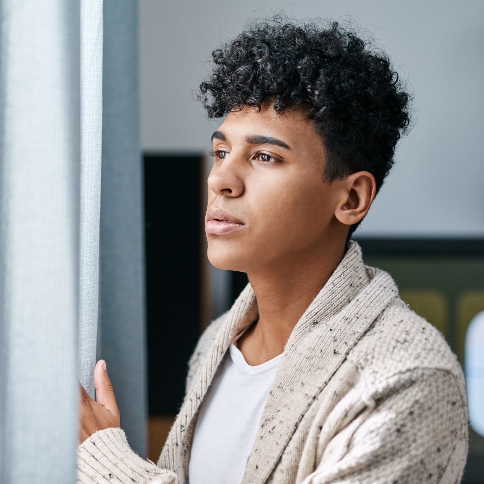 Home, thinking and man by window with social anxiety, reflection or winter burnout. Depression, mental health and tired person in bedroom for emotional stress, decision or planning in apartment