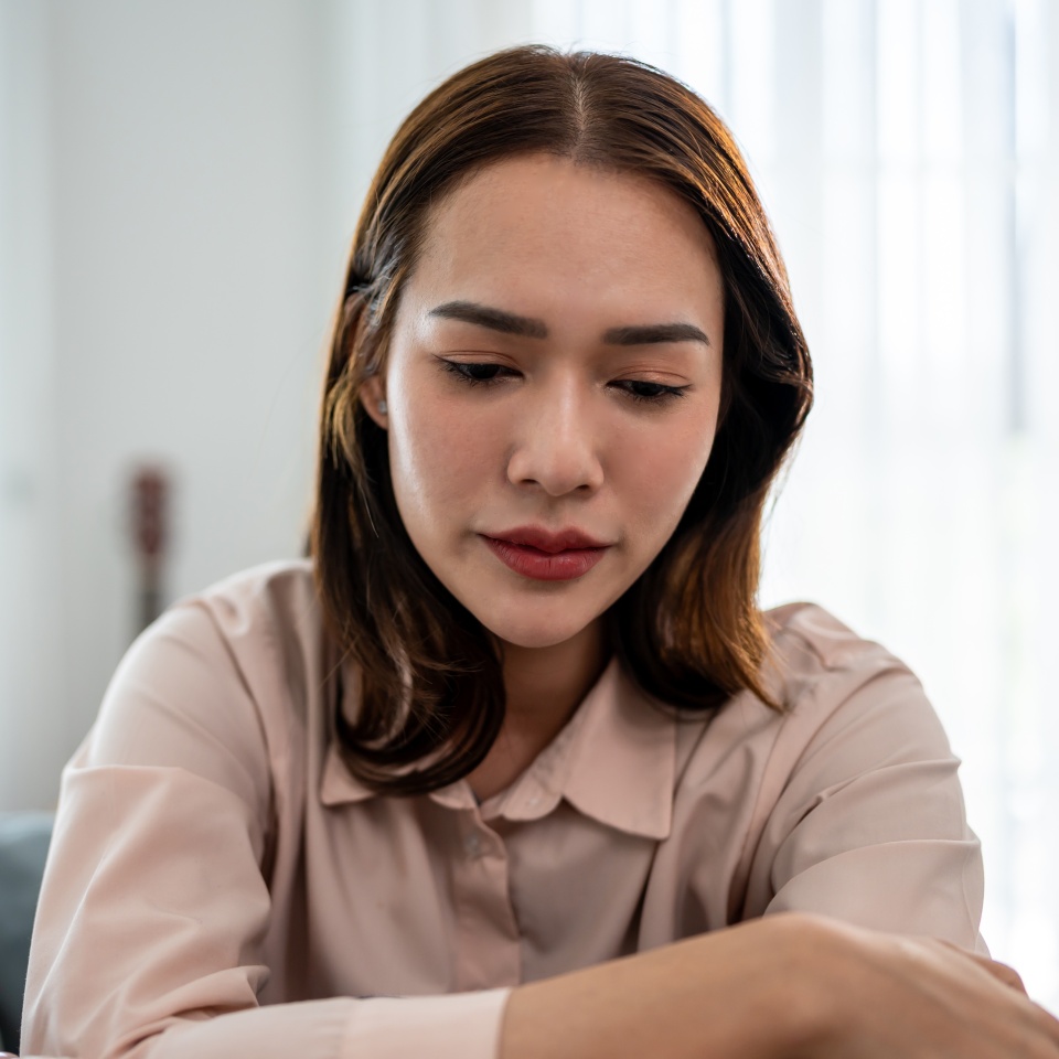 Asian upset depressed woman sitting alone on sofa in living room at home. Attractive unhappy young femlae feeling sad, lonely and upset with life problem then crying with tears in quiet room in house.