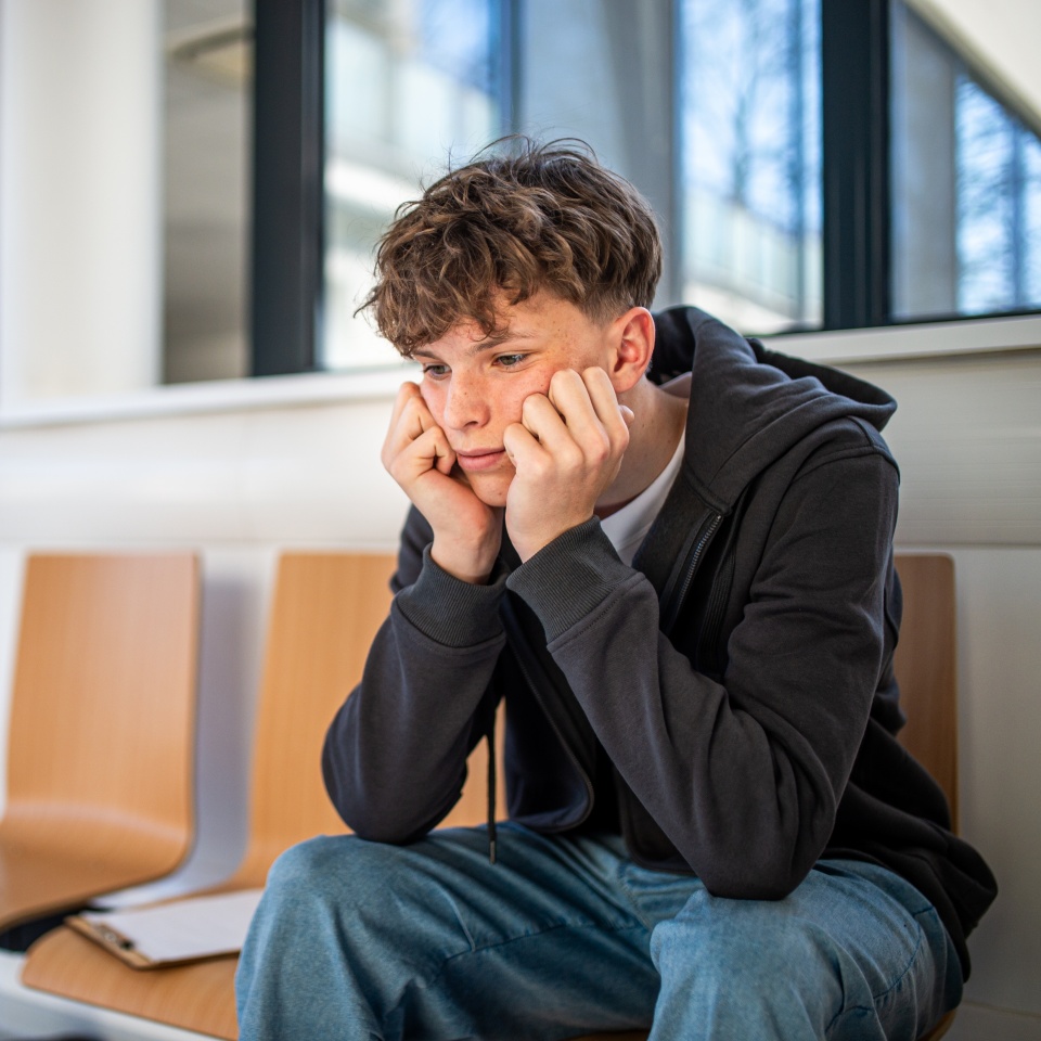 Anxious teenager waiting alone in hospital waiting area before medical checkup.
