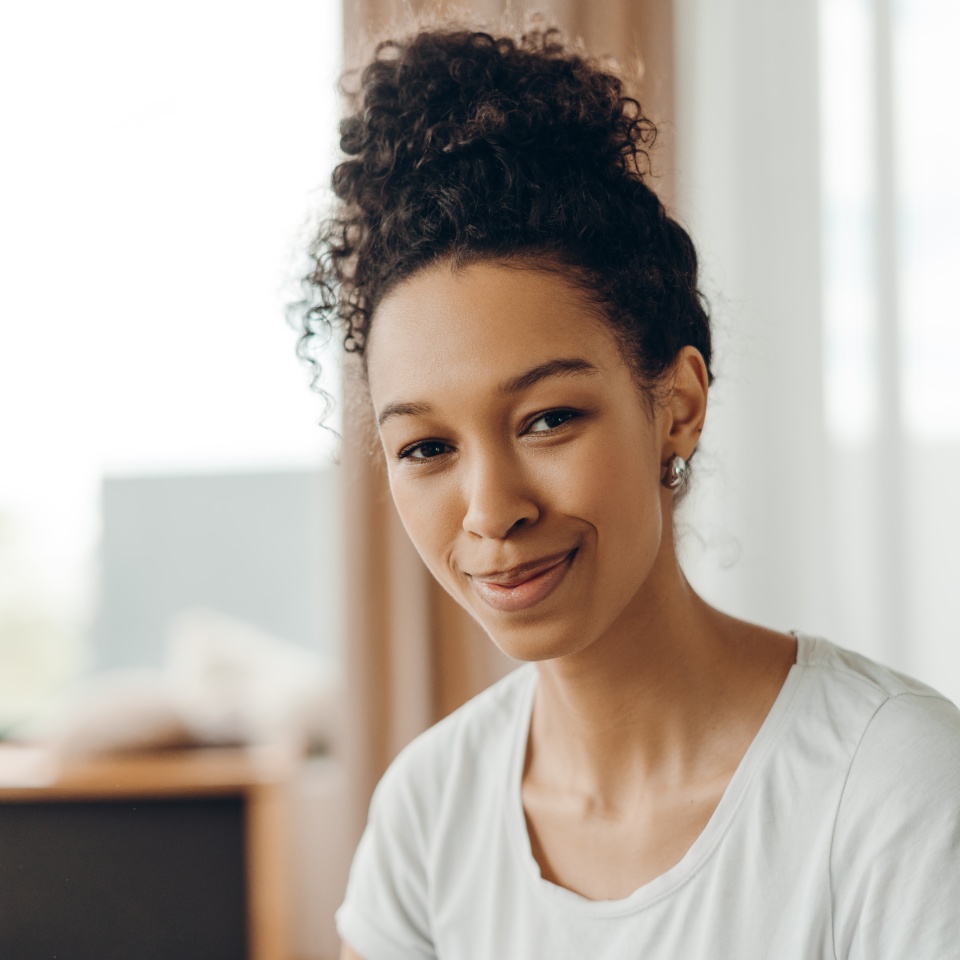 Portrait of beautiful young African American woman with natural curly hair and casual outfit sitting at home, calmly looking into the camera. Lifestyle concept