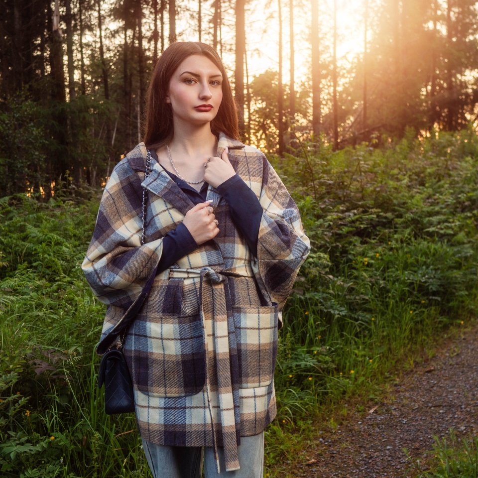 Portrait of a stylish young girl in a park at sunset. Fashion and beauty. Enthusiastic model with long hair and slim body type wearing luxury outfit. Calm and relaxed mood.