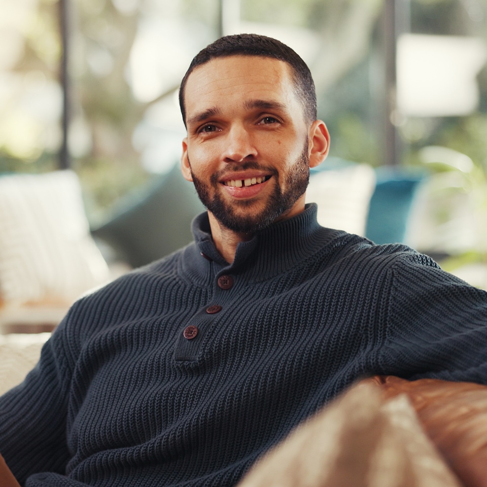 Happy, portrait and man on sofa with pride, confidence and relaxing break on weekend getaway. Smile, positive attitude and person on couch for calm holiday, vacation and wellness in living room.