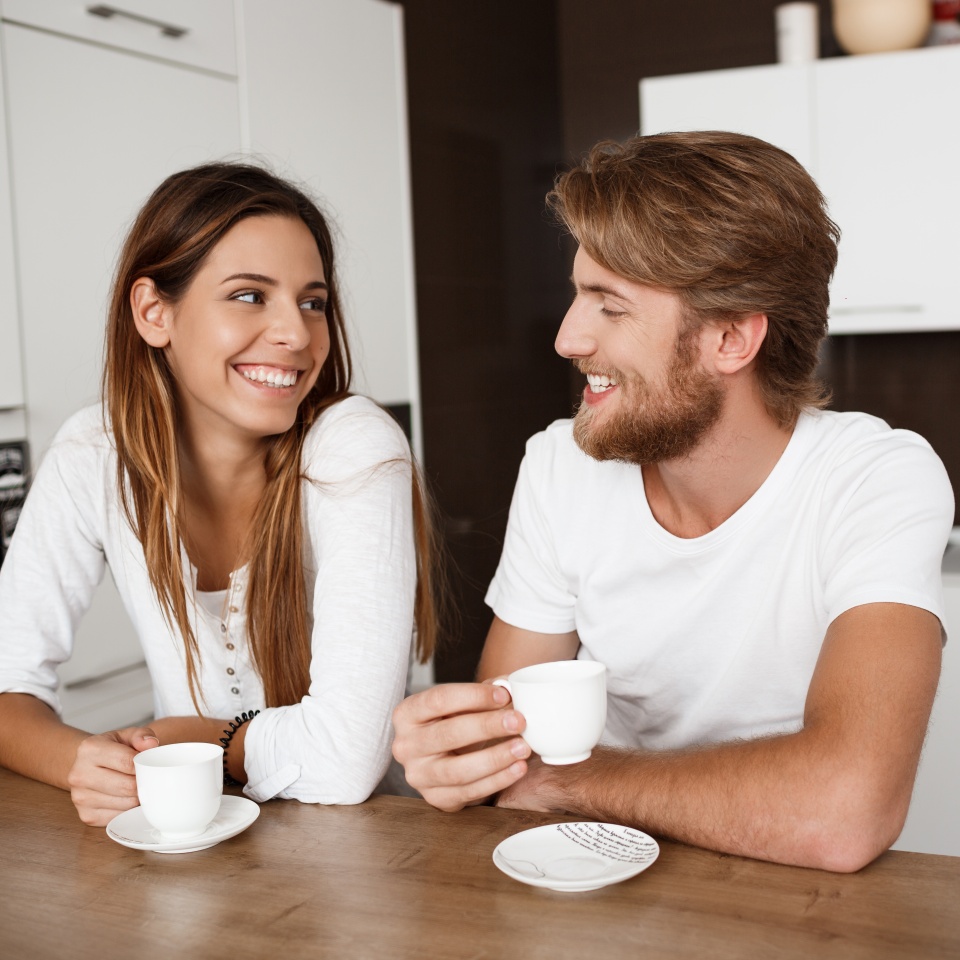 Young beautiful couple sitting at kitchen drinking morning coffee smiling.