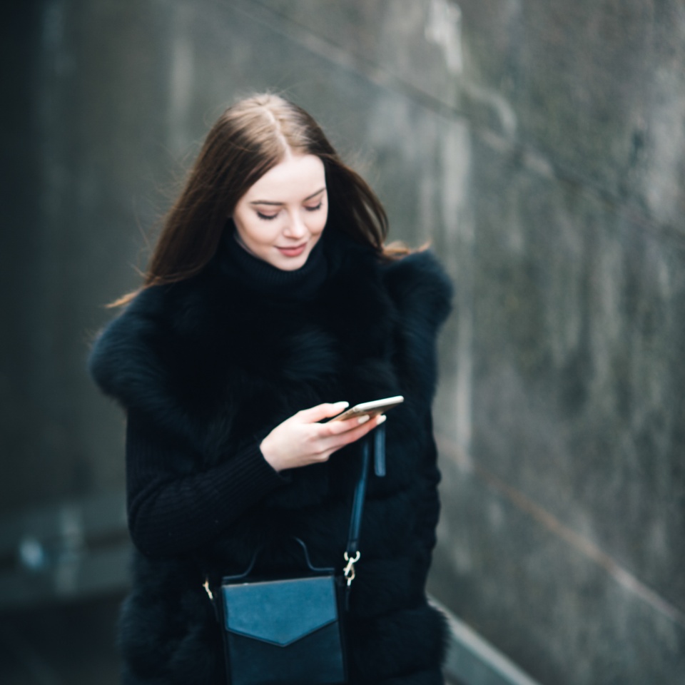Cheerful young model in winter clothes holding her mobile phone outside on a cloudy day beautiful woman
