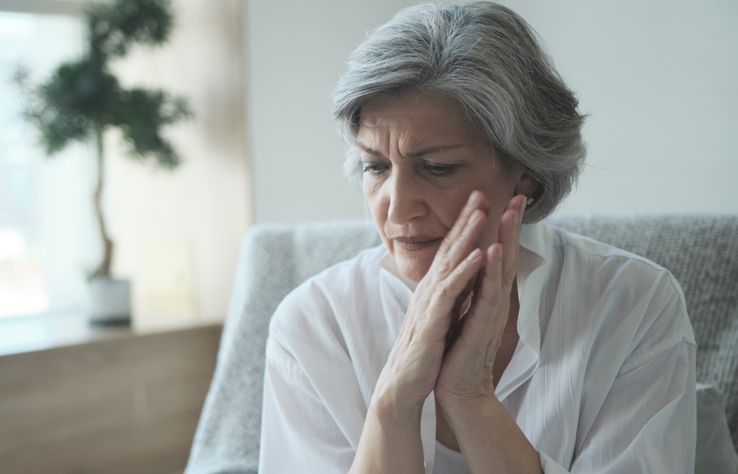 Elderly senior woman massaging her temples to reduce her headache. Older lady feeling scared, anxious, and thinking of sickness or mental health while suffering from a severe migraine or memory loss.